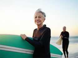 An older couple with surfboards walking along the beach at sunset