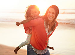 A mother giving her daughter a piggyback ride at the beach at sunset